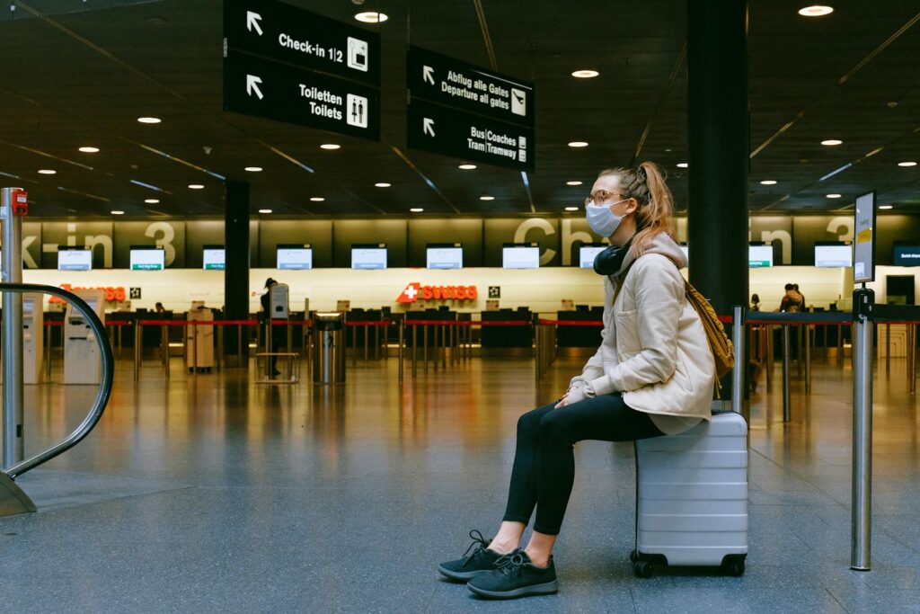 A woman wearing a face mask sits on luggage in an airport terminal amid the pandemic.