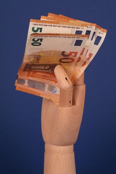 Wooden dummy hand holding euro banknotes against a blue background.